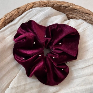 Detail of burgundy velvet scrunchie with silver bead accents on rustic linen background