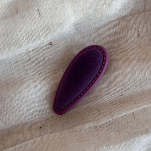 Detailed close-up of dark purple velvet teardrop hair clip on a textured linen fabric