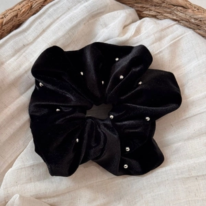 Detailed view of black velvet scrunchie decorated with silver beads on a fabric background