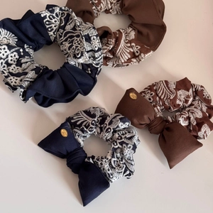 Close-up of navy and coffee scrunchies with white embroidery and golden bow logos