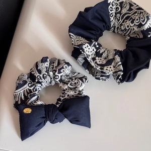 Detail of navy blue knit scrunchies with white embroidery and golden metal logo charm