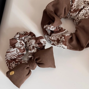 Detailed macro view of two brown knit scrunchies with white embroidery and golden metal tag