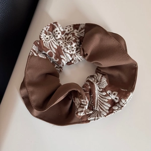 Detailed view of dark brown knitted scrunchie with white floral embroidery patterns