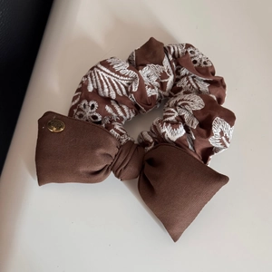 Close-up of brown scrunchie with floral embroidery and golden logo metal detail