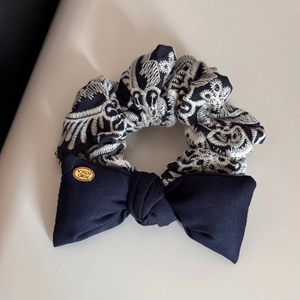 Detail of navy blue bow hair tie with vintage embroidered pattern and gold logo charm