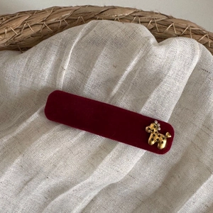 Detail of a dark red velvet hair clip with a vintage golden poodle metal charm