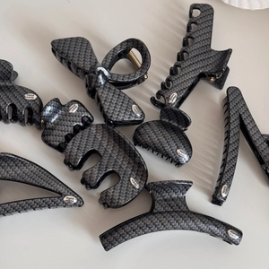 Detail of carbon fiber texture hair claw clips with handmade silver label on grey background