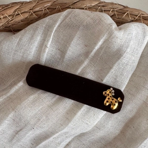 Detail of a dark brown velvet rectangular hair clip with a golden poodle charm
