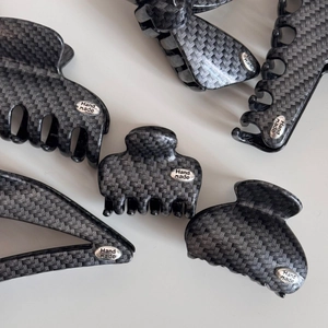 Detail of five grey carbon fiber hair claws with 'Hand Made' silver metal plates