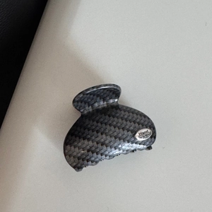 Detailed close-up of dark grey carbon fiber pattern hair claw with silver Hand Made plaque