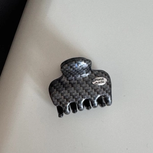 Macro detail of dark grey hair claw clip featuring carbon fiber texture and Hand Made plaque