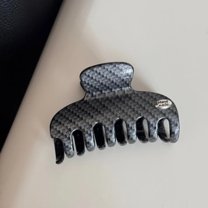Close-up of gray carbon fiber texture hair claw clip with silver Hand Made metal emblem