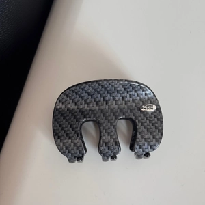 Detailed view of the carbon fiber texture hair claw clip with a silver handmade logo plate