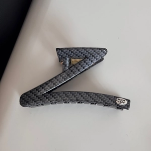 Detailed close-up of dark grey carbon fiber texture on Z-shaped hair claw clip with handmade tag