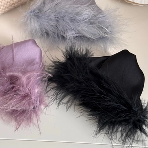 Detail view of premium hair clips with soft feathers and satin fabric in purple, black and grey