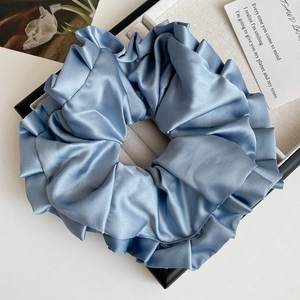 Détail macro d'un grand chouchou en satin plissé bleu clair présenté dans un coffret