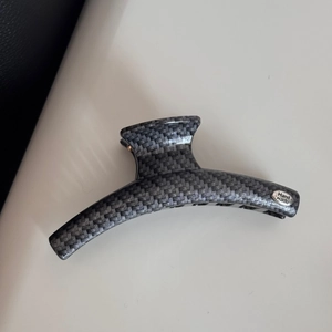 Detail of grey hair claw clip showing carbon fiber texture and silver Hand Made plaque