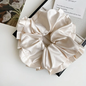 Gros plan d'un chouchou en satin crème avec texture plissée soyeuse sur plateau de luxe