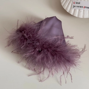 Detail of purple satin hair claw clip with fluffy feathers on a minimalist gray surface