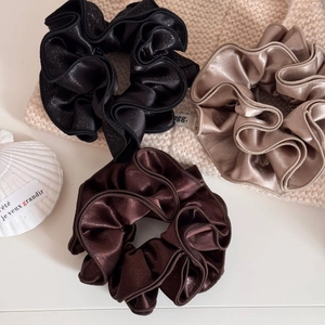 Detailed view of three satin scrunchies in black, coffee, and champagne with glitter texture