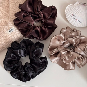 Close-up of three satin scrunchies in black, brown and gold with subtle glitter texture