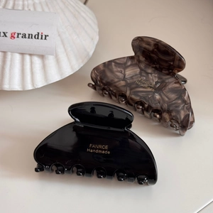 Detail view of handmade black and amber fan-shaped hair claws with gold logo