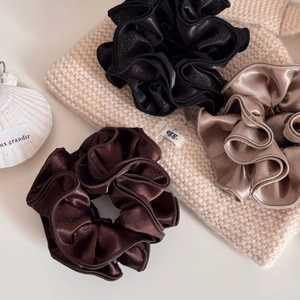 Three oversized shimmering satin scrunchies in earthy tones on a beige knit sweater