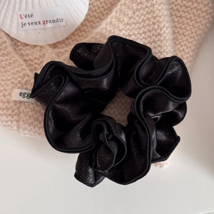 Detail of black satin scrunchie with silver glitter and white woven egg brand label