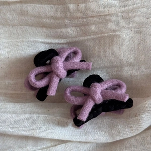 Détail de deux mini barrettes à nœud en feutre de laine violet sur tissu blanc texturé