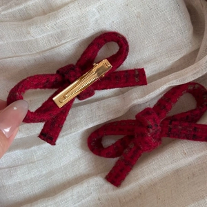 Detail of red wool bow hair clips with golden alligator fasteners on linen background