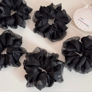 Close-up of set of five black satin scrunchies with sheer organza edges and silver glitter