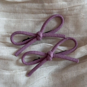 Détail de barrettes à cheveux nœud en laine violette sur tissu beige texturé doux