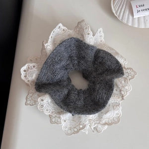 Detail eines dunkelgrauen Strick-Scrunchies mit weißem Spitzenbesatz und Muschel-Deko