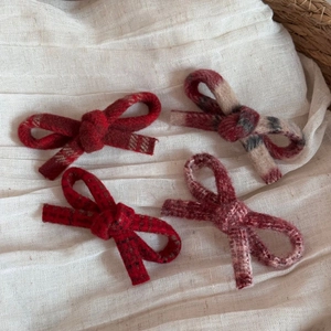 Set of four elegant tweed bow hair clips in various red patterns on a soft fabric background