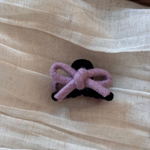 Vue détaillée d'une pince à cheveux avec nœud en laine lilas et base noire sur tissu en lin