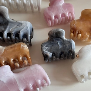 Detailed macro of acetate hair claws in marble grey, pink, and amber with smooth finish