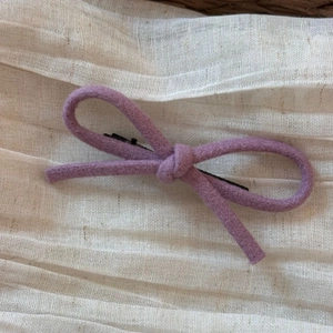 Détail de la pince à cheveux nœud en laine violette sur tissu plissé beige doux