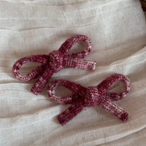 Close-up of two burgundy tweed bow hair clips on a soft textured cream fabric