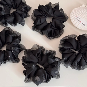 Detail of five black satin scrunchies with sequin mesh edges on a minimalist table