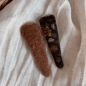 Détail de barrettes BB à fleurs et pinces en feutre marron sur tissu beige