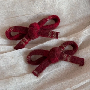 Macro detail of red wool bow hair clips featuring a vintage plaid pattern on cream fabric
