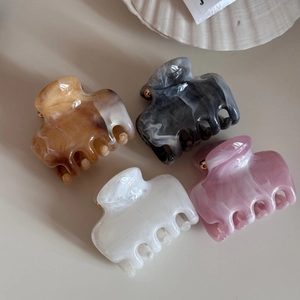 Close-up of four marble-patterned acetate hair claws in amber, gray, white, and pink