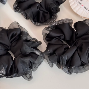 Macro detail of black satin scrunchies with silver glitter mesh edges and ruffled texture