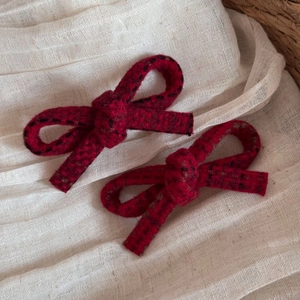 Detail view of two red plaid wool bow hair clips on a beige textured linen background