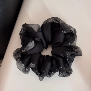 Detailed close-up of a black satin scrunchie featuring rhinestone edges and organza trim