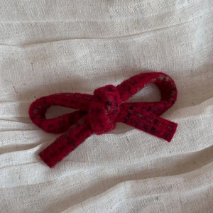 Close-up of red plaid tweed bow hair clip with detailed woven fabric texture on linen