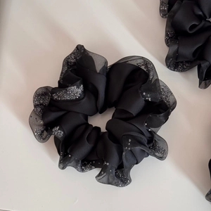 Close-up of black satin scrunchie with sheer mesh edges and shimmering silver rhinestones