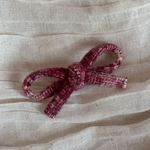 Close-up of a burgundy tweed bow hair clip on a soft textured fabric background