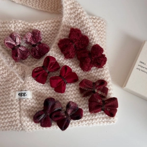 Lot de 10 barrettes à nœuds rouges en laine aux motifs variés sur un fond en maille