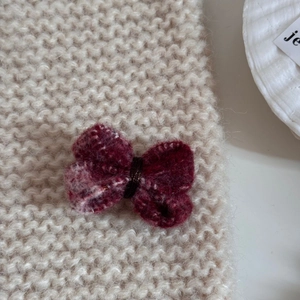Gros plan d'une pince à cheveux nœud en laine rouge foncé sur un fond crème texturé